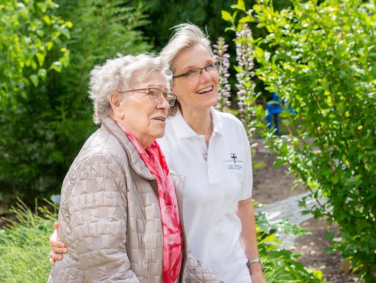 Im Garten: eine Pflegerin zeigt einer Bewohnerin etwas (nicht sichtbar)