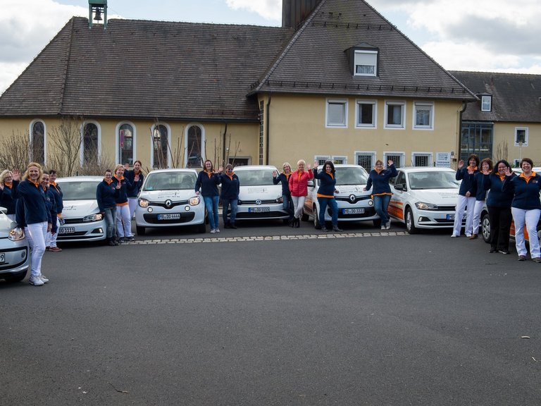 Gruppenfoto mit KFZ-Fahrzeugflotte: Frauen die vor ihren Fahrzeugen stehen und winken
